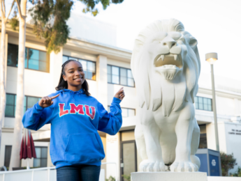 A student in an LMU sweatshirt points to a lion statue on campus.