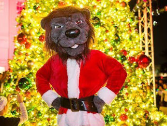 Iggy the LMU Lion in front of the Campus Christmas tree in Santa Gear