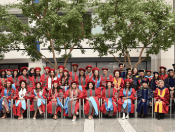 Doctoral graduates and faculty wearing commencement regalia and sitting in an indoor courtyard
