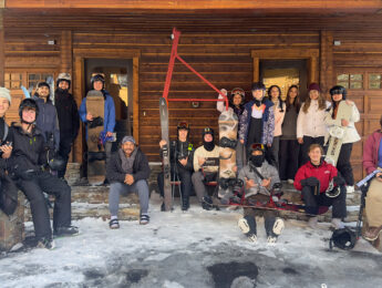 Students gather outside of a wood cabin dressed in winter gear at Mammoth Mountain.