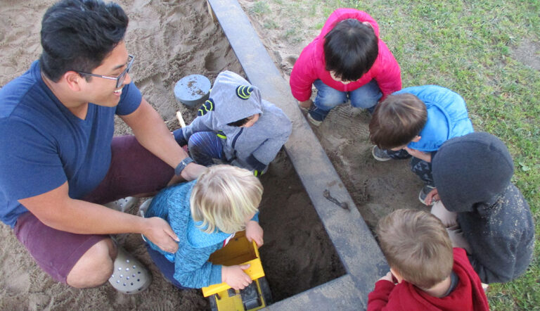 toddlers playing with a teacher in a sandbox