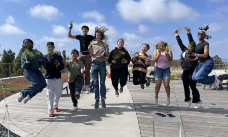 Students holding plants and jumping mid-air.