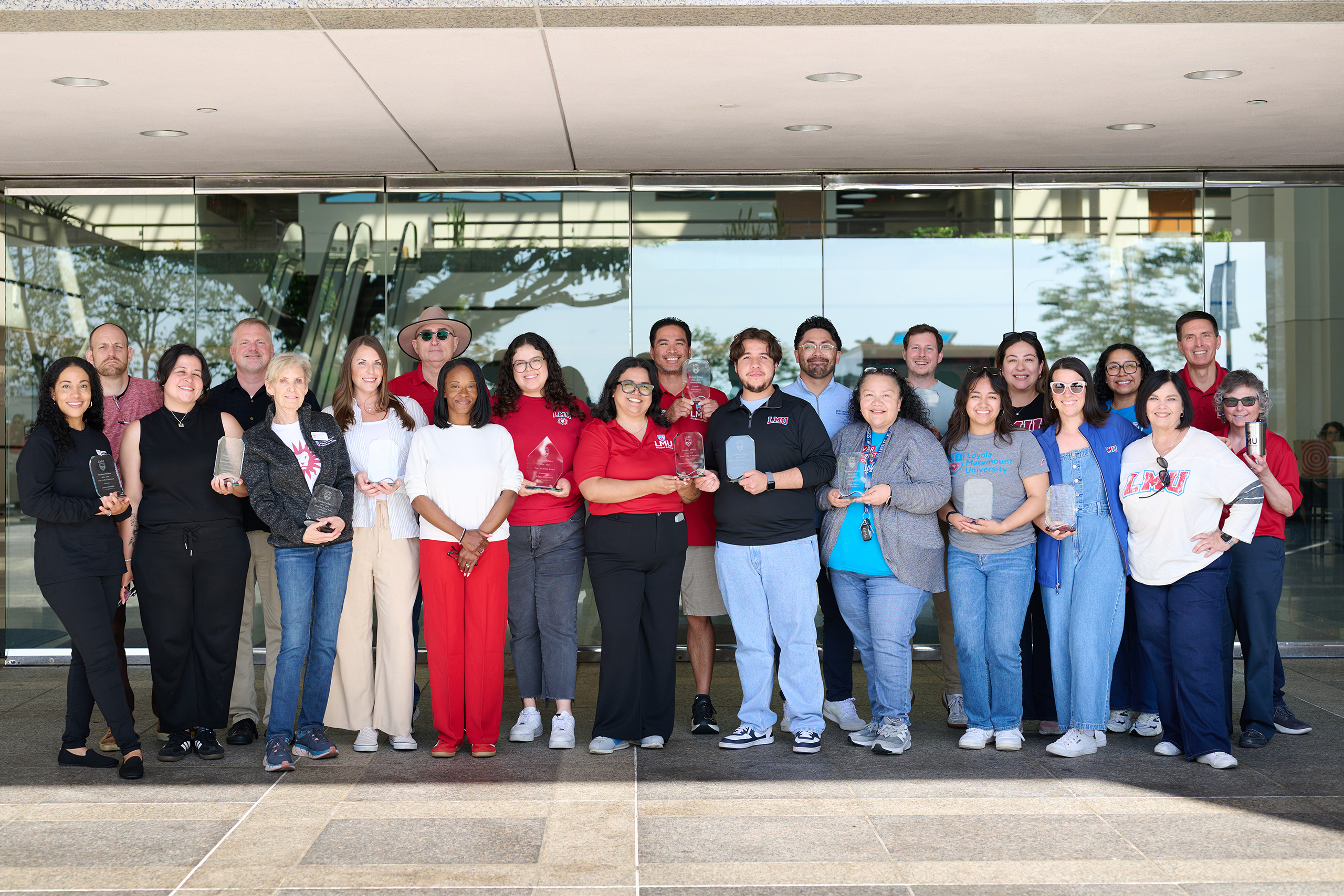 Student Affairs staff stand outside in front of glass doors holding awards.