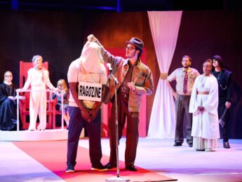 Ragozine stands in handcuffs and a man begins to remove the hood from his head. They stand in front of a judging panel.