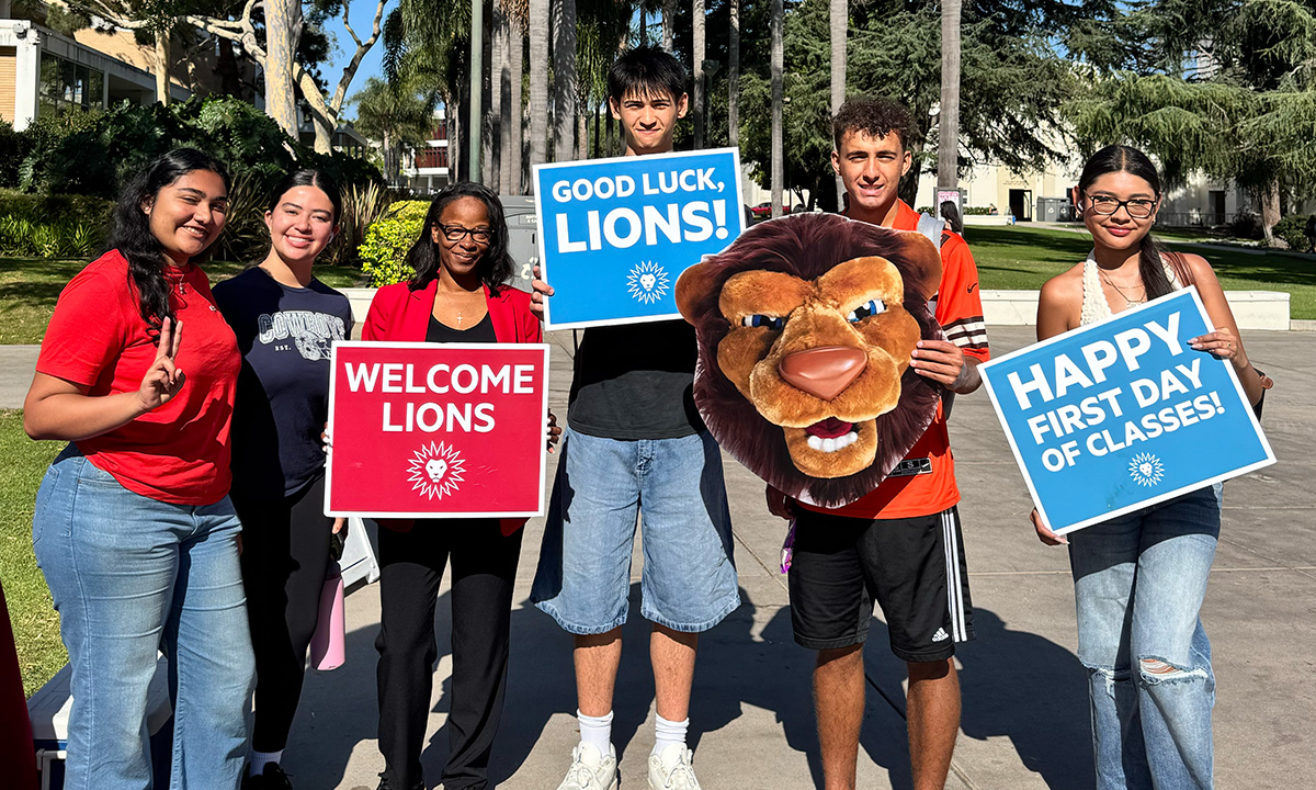 Students pose with SVP Leggett on the first day of classes holding red and blue signs that say "Welcome Lions" and "Happy First Day of Classes."