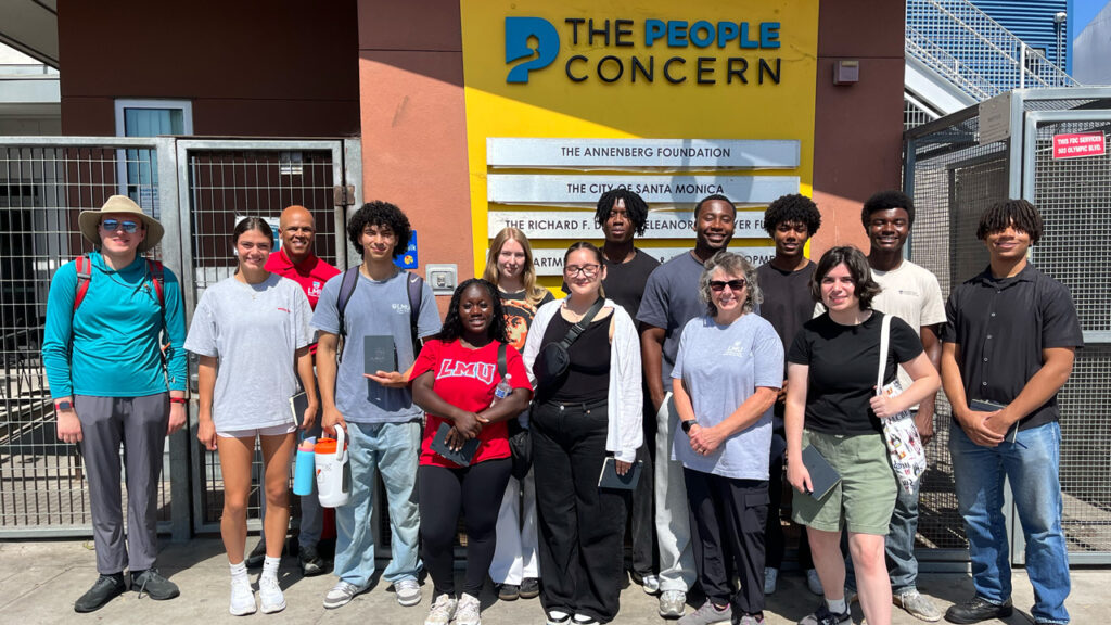 Students and staff members stand outside in front of a yellow sign for The People Concern.
