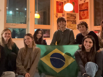 Students gather around dim light holding a Brazilian flag.