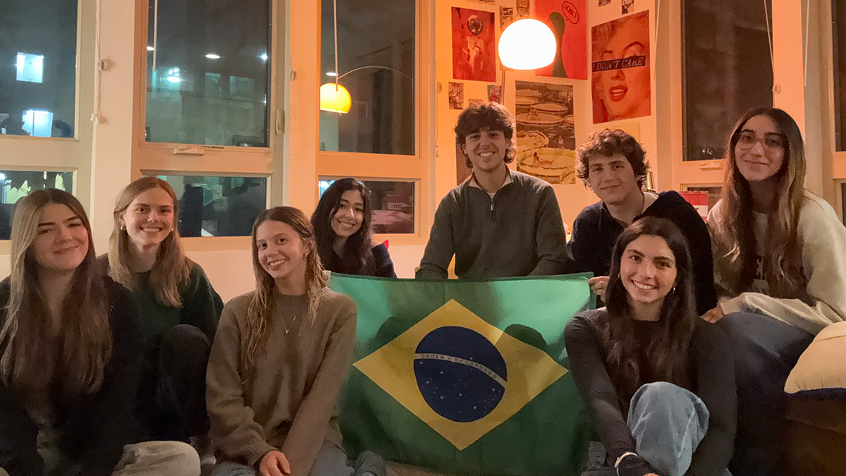Students gather around dim light holding a Brazilian flag.