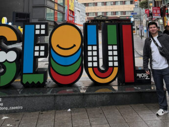 Jose Rodriguez-Alcorta stands outside in front of a colorful sign that says SEOUL while travelling in Korea.