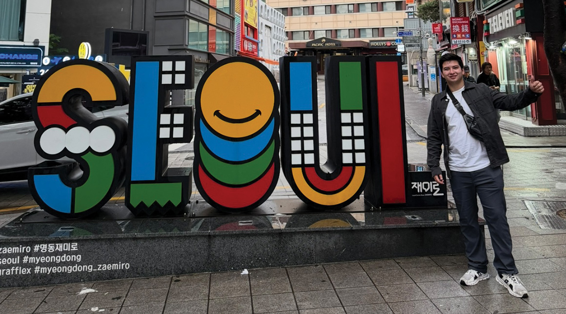 Jose Rodriguez-Alcorta stands outside in front of a colorful sign that says SEOUL while travelling in Korea.