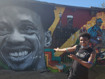 A student stands outside in front of a colorful mural on a global immersion trip.