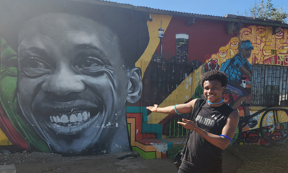 A student stands outside in front of a colorful mural on a global immersion trip.