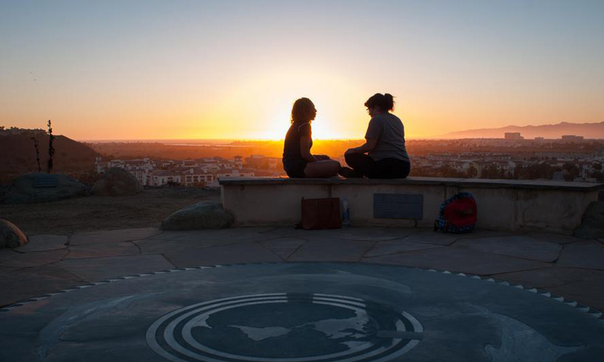 Two students sit on the bluff in the Garden of Slow Time during sunset having a conversation.