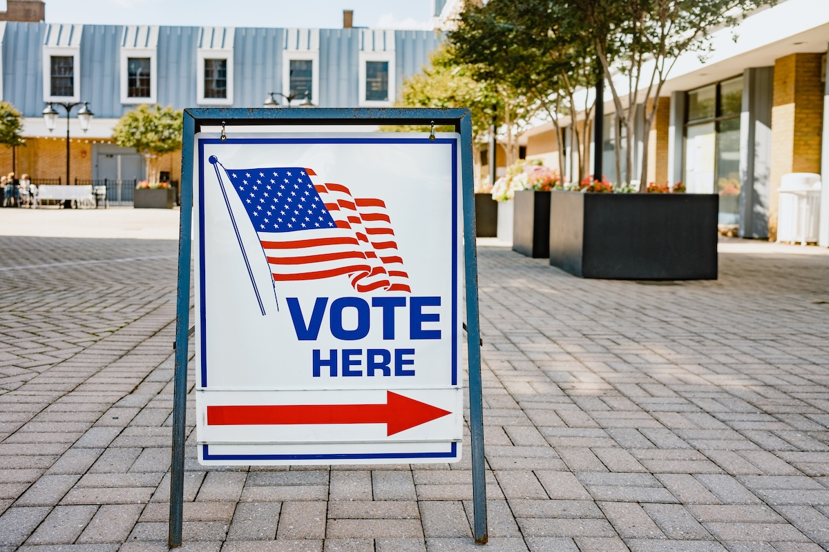 "Vote Here" Sign pointing to the right in front of a building