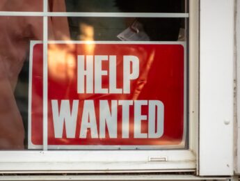 A red "HELP WANTED" sign displayed prominently in a store window, signaling the business's need for additional staff.
