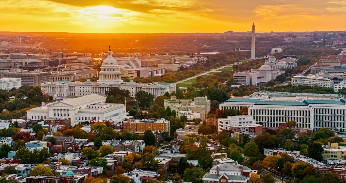 Helicopter shot of Capitol Hill in Washington, D.C. at sunset on a fall evening, looking over residential streets towards the U.S. Capitol Building, Supreme Court, and the National Mall.