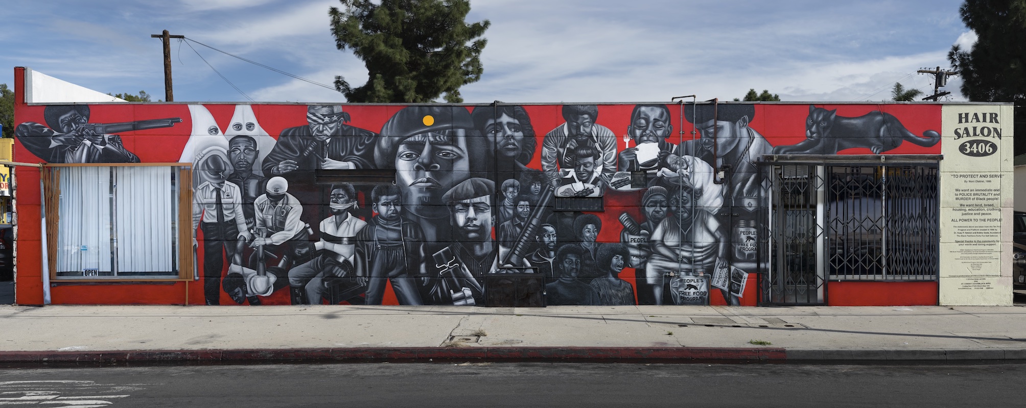Mural in black, white and red depicting faces and figures of people on the side of a building. Image credit: Noni Olabisi, "To Protect and Serve," 1995, Acrylic, 12 x 40 ft., 11th Ave. at Jefferson Blvd. Photo credit: Social and Public Art Resource Center (SPARC), The Great Walls Unlimited: Neighborhood Pride Mural Program, 1988-2002, Courtesy of Laband Art Gallery, Copyright held by the Estate of Noni Olabisi