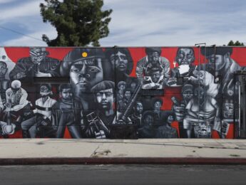 Mural in black, white and red depicting faces and figures of people on the side of a building. Image credit: Noni Olabisi, "To Protect and Serve," 1995, Acrylic, 12 x 40 ft., 11th Ave. at Jefferson Blvd. Photo credit: Social and Public Art Resource Center (SPARC), The Great Walls Unlimited: Neighborhood Pride Mural Program, 1988-2002, Courtesy of Laband Art Gallery, Copyright held by the Estate of Noni Olabisi