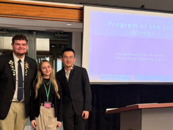 Three students pose near a projector at a student-led conference to receive the program of the year award.