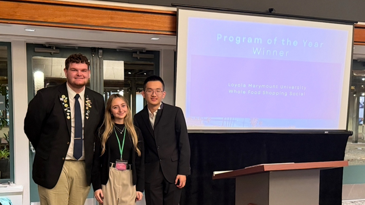 Three students pose near a projector at a student-led conference to receive the program of the year award.