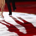 Winter Sports Concept. Figure Skating Elements. Low Section Of Unknown Ice Dancing Couple With Illuminating Ice Reflection, Copy Space, Neon Lighting