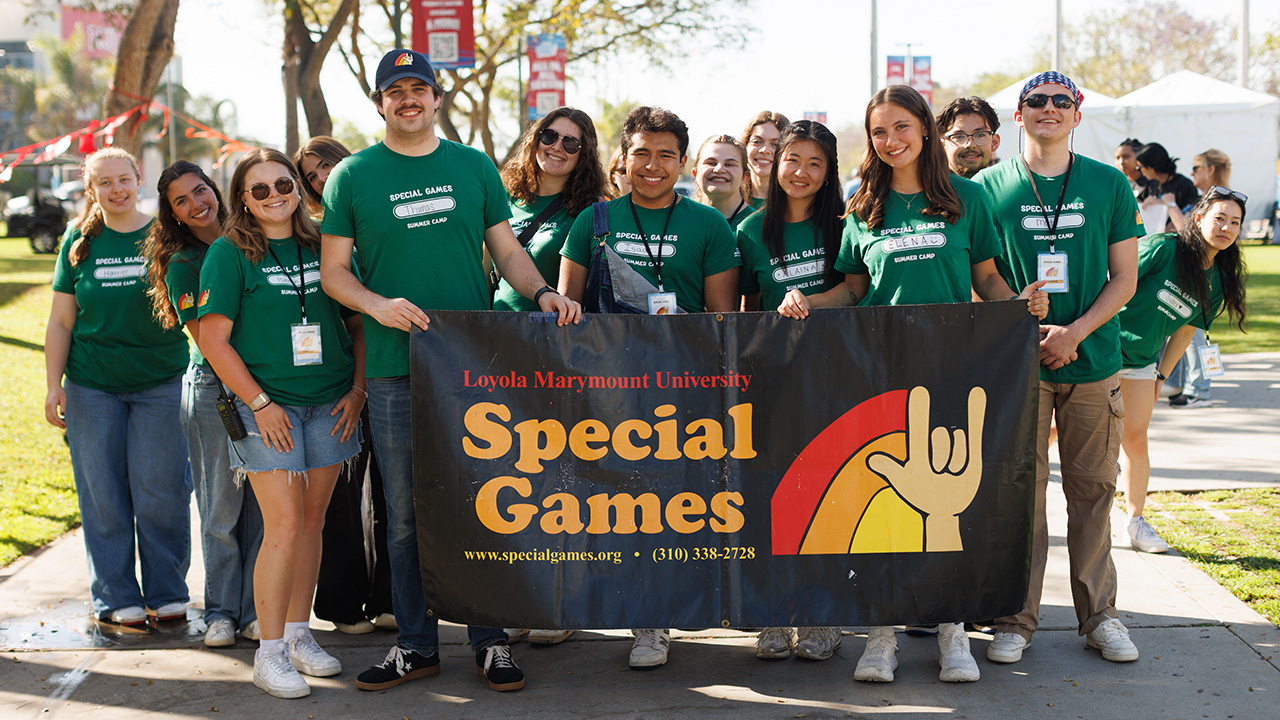 Student leaders pose in green T-shirts in front of a black banner with the Special Games red, orange, and yellow logo.