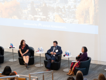 two women and two men sitting in leather chairs in front of an audience with white tables between them and an LMU banner to the right of them.