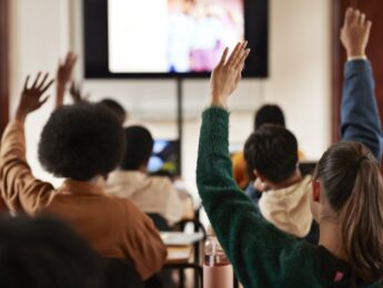 Rear view of students with hands raised in classroom