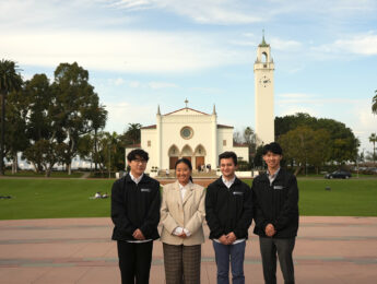 Students and a staff member pose in front of Sacred Heart Chapel on Regents Terrace