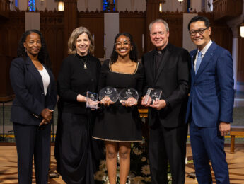 A student wearing a black dress poses with staff and administrators to receive the Class of 2026 Valedictorian and other awards at the annual student award ceremony