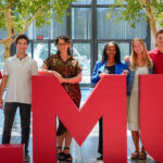 Students and staff pose behind the red LMU letters inside University Hall