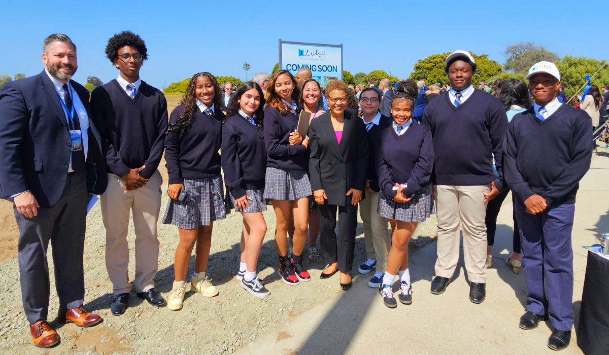 Catholic school students of high school age wearing uniforms and stand with some adults at a construction site in Los Angeles
