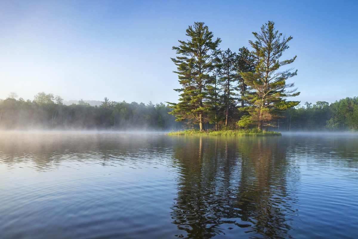 Beautiful calm blue lake and island with pine trees and fog on a summer morning in northern Minnesota