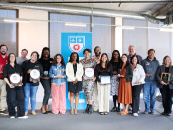 Staff gather on a grey carpeted stage who were honored with the annual Pillar Awards with an LMU blue banner in the center behind them