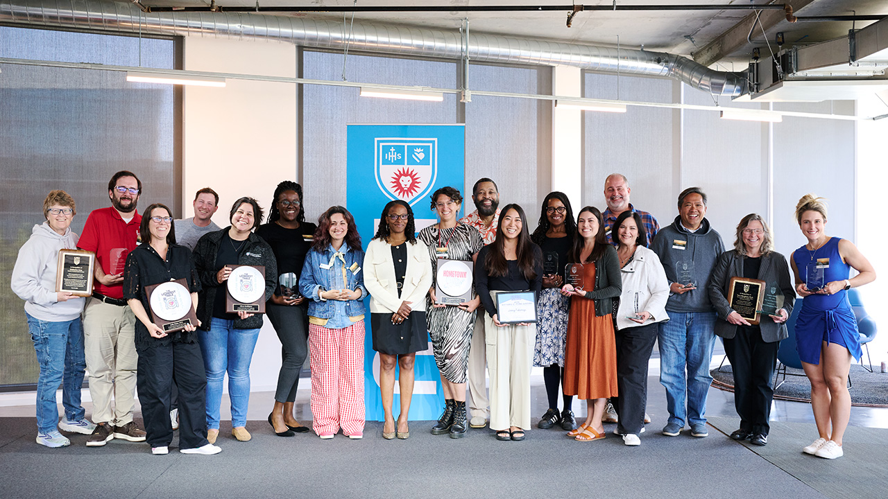 Staff gather on a grey carpeted stage who were honored with the annual Pillar Awards with an LMU blue banner in the center behind them