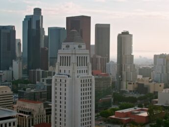 Aerial shot of Los Angeles City Hall in Downtown Los Angeles with financial district skyscrapers in background at sunset.