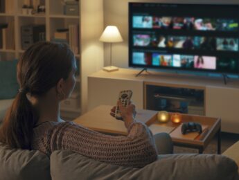 Woman relaxing on the couch, she is using the remote control and choosing a TV show or movie on the television menu