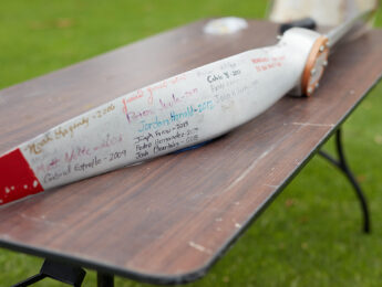 A ceremonial aircraft wing rests on a wooden table outdoors covered with handwritten names and years dating from 2006 to 2017
