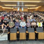 Group photo of about 100 faculty members seated in auditorium