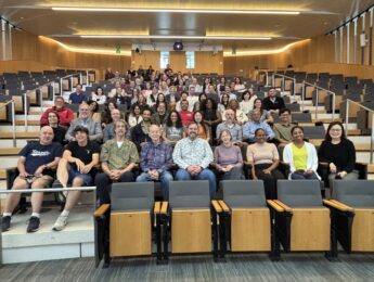 Group photo of about 100 faculty members seated in auditorium