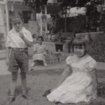 Siblings Lawrence “Buddy” (left) and Carol (right) are in the foreground, while their neighbor Lolita (middle) sits with the family dog, Blondie, on a raised cement flower planter in their lawn under an avocado tree. Courtesy Carol Jacques, Chavez Ravine: An Unfinished Story archival collection