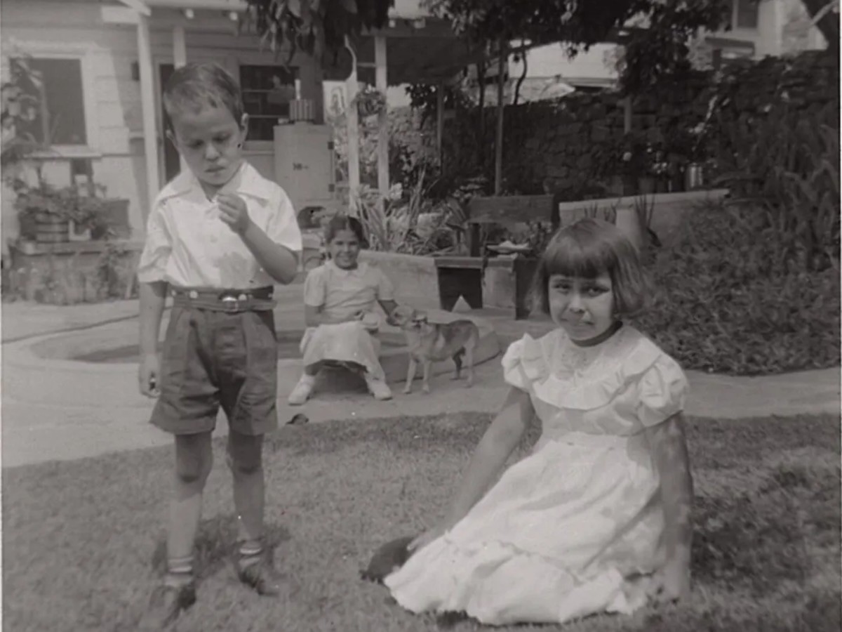 Siblings Lawrence “Buddy” (left) and Carol (right) are in the foreground, while their neighbor Lolita (middle) sits with the family dog, Blondie, on a raised cement flower planter in their lawn under an avocado tree. Courtesy Carol Jacques, Chavez Ravine: An Unfinished Story archival collection