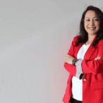 woman wearing a red blazer and a white shirt standing against a tan background
