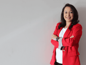 woman wearing a red blazer and a white shirt standing against a tan background