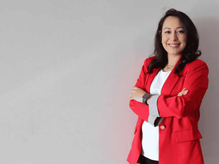 woman wearing a red blazer and a white shirt standing against a tan background