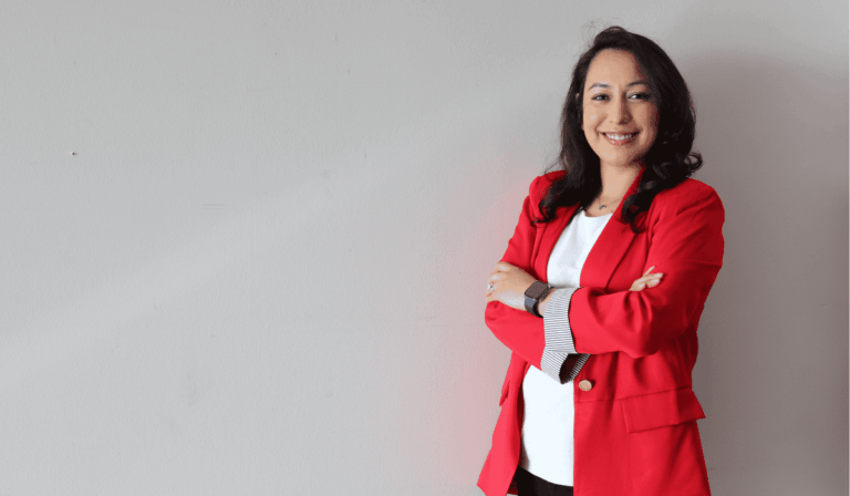 woman wearing a red blazer and a white shirt standing against a tan background