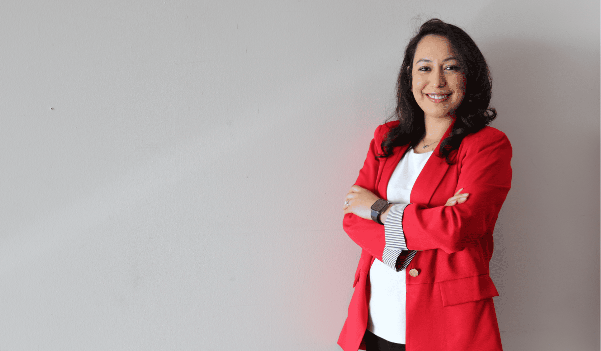 woman wearing a red blazer and a white shirt standing against a tan background