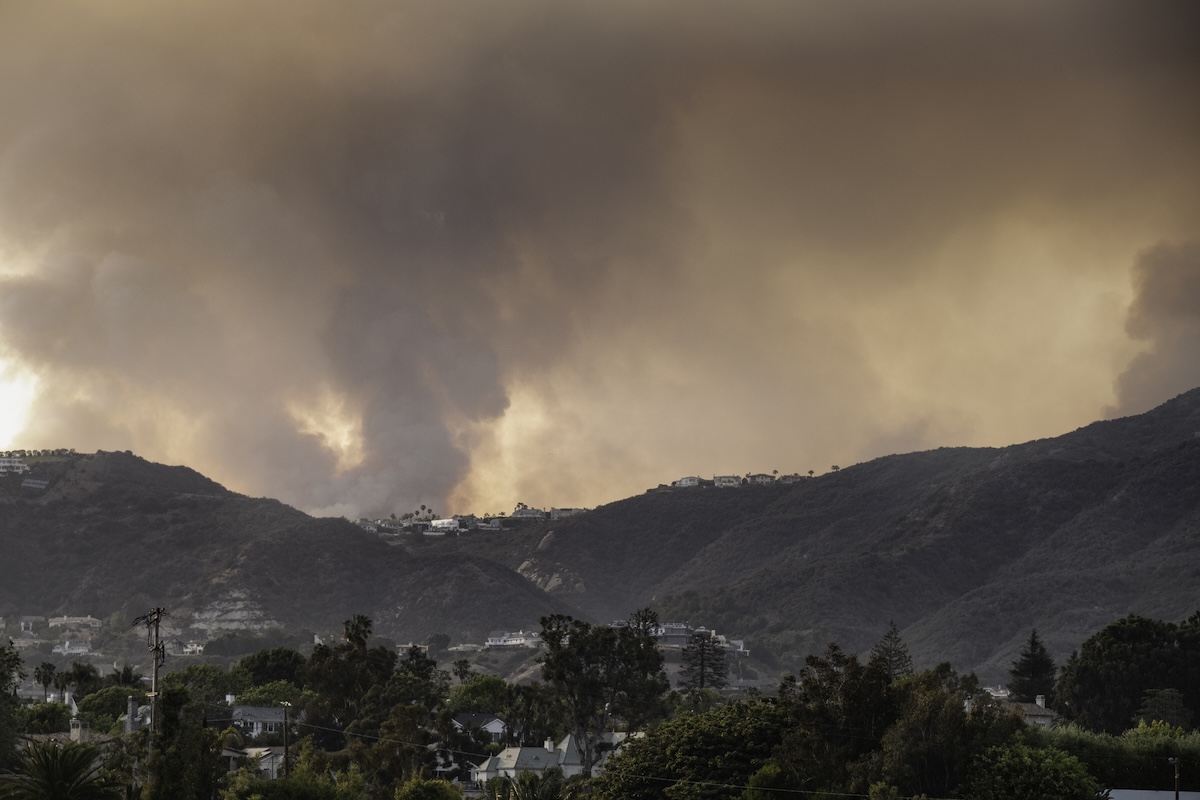 View from Santa Monica of wild fire in Pacific Palisades, a suburb of Los Angeles, in the Santa Monica mountains. The fire is burning in mountainous terrain densely covered by chaparral brush, and is close to many homes