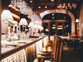 Stylish restaurant bar counter with soft lighting, glassware, and wooden chairs, creating a cozy and refined dining atmosphere. The image symbolizes hospitality, fine dining, nightlife, and a modern lifestyle.