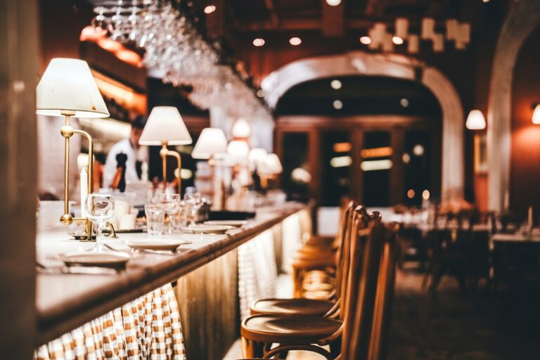 Stylish restaurant bar counter with soft lighting, glassware, and wooden chairs, creating a cozy and refined dining atmosphere. The image symbolizes hospitality, fine dining, nightlife, and a modern lifestyle.